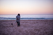 © rushay - Woman taking her dog for a walk on beach during dusk