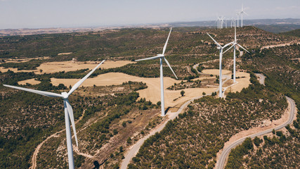 Group of wind turbines at a wind farm on a hill with some fields in summer. Ecology concept