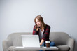 © Богдан Маліцький - young girl with a laptop sitting on the couch and drinking coffee, a woman using a computer against a white blank wall, she freelancing and printing text, copy space