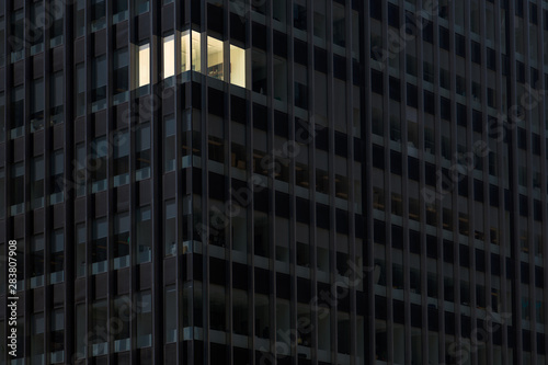 Fotomural Corner office with lights on and windows glowing in a darkened office building a