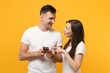 © ViDi Studio - Beautiful young couple friends guy girl in white empty blank t-shirts posing isolated on yellow orange background. People lifestyle concept. Mock up copy space. Using mobile phone, typing sms message.