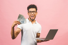 Closeup Portrait, Young Successful African American Business Man Making Money From Internet, Holding Cash In Hand, Laptop In Another, Isolated Over Pink Background.