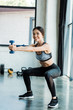 © LIGHTFIELD STUDIOS - positive young sportswoman holding dumbbells and doing squat exercise