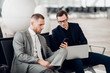 © romankosolapov - Young businessman showing a text message on his mobile phone to a male colleague at airport