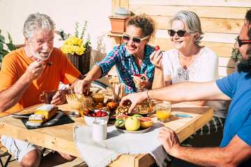 group of happy people having breakfast at home in the terrace together with love - faughter, son, grandma and grandpa eating and drinking - couple of seniors married and adults