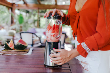 Wall Mural - young woman preparing a healthy recipe of diverse fruits, watermelon, orange and blackberries. Using a mixer. Homemade, indoors, healthy lifestyle