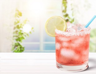 Delicious pink cocktail with ice and lemon on blurred background