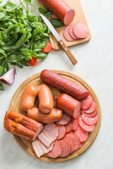 Wooden board with assortment of sausages on light table