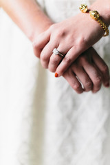 close up of bride holding her hands, gold bracelet, big diamond ring, textured wedding dress