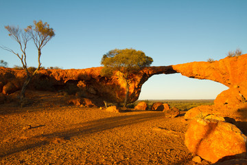 Sandstone archway looking out on the Australian outback. Early morning light playing across the arid orange sand