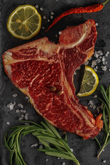 Wall Mural - Raw fresh beef T-bone steak and seasoning on dark background. Top view.