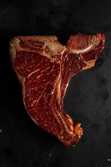 Wall Mural - Raw fresh beef T-bone steak on dark background. Top view.