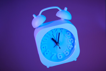 Light blue alarm clock suspended in air on a bright purple background