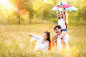 Asian family father, mother and daughter play ta kite in the outdoor park