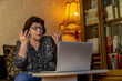 © Dmitrii - Senior woman in a glasses spreads her arms up. She sits in front of computer and very indignant. Laptop on the white table. Using technology in old age concept