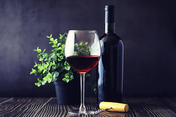 A glass of red dry wine on the table. Dark bottle and glass of wine.