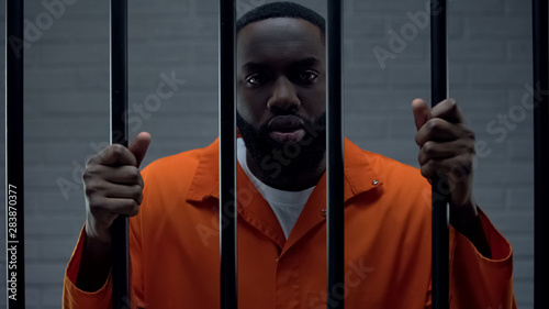 Fotografía Black prisoner holding bars and looking at camera, drug dealer punishment