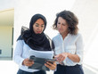 © Mangostar - Focused female managers studying reports. Arab and Caucasian women standing and reading documents together. Paperwork concept