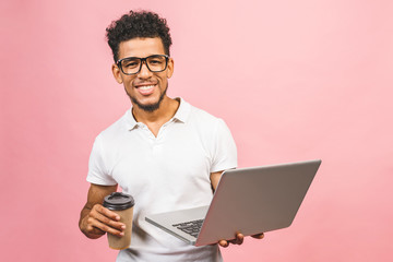 Using laptop. Portrait of handsome casual african american young man drinking coffee while holding laptop computer isolated against pink background.