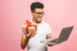 © denis_vermenko - Portrait of happy young afroamerican man using laptop comruter, gift box  and checkin isolated against pink