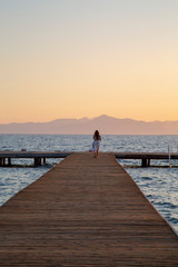 Wall Mural - Girl on pontoon pier at sunset . Woman relaxing on pier looking at sea view at sunset