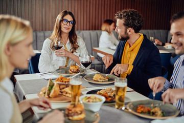 Poster - Multiethnic friends sitting at restaurant, drinking alcohol, chatting and having burgers for dinner.