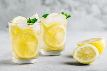 Lemonade With Lemon, Mint And Ice Cubes In Glass On Gray Stone Background.
