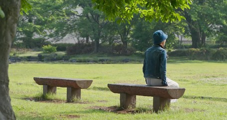 Canvas Print - Woman sit on the wooden bench and look around in the park