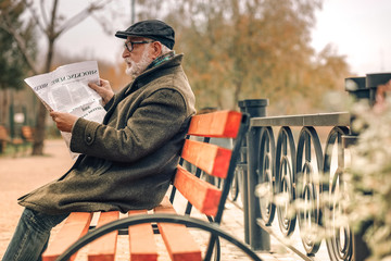 Side view of a senior man reading newspaper in park