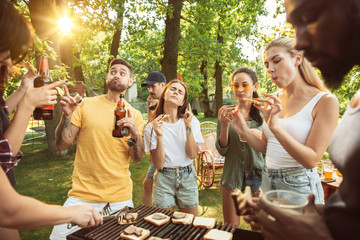 Group of happy friends having beer and barbecue party at sunny day. Resting together outdoor in a forest glade or backyard. Celebrating and relaxing, laughting. Summer lifestyle, friendship concept.