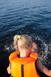 blond little girl in life vest swimming in the sea, pool. sunny day. close up. view from the back