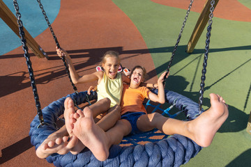 Two girls joyfully and cheerfully ride on a large hanging swing in the playground