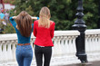 Two slim girls walking in a summer city, rear view. Sexy women in jeans with perfect hairstyles, concept of female fashion and friendship
