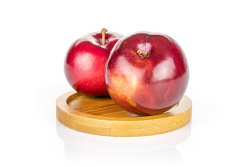 Group of two whole ripe red round plum on round bamboo coaster isolated on white background