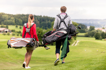 Rear view of couple carrying golf bag