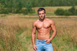 Caucasian shirtless man brunet with a tanned shirtless body in jeans stands on a country road.