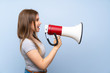 © luismolinero - Teenager girl over isolated blue wall shouting through a megaphone