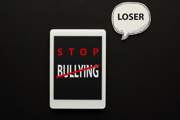 top view of digital tablet with stop bullying lettering on screen on black background near white speech bubble with loser word