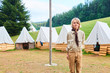Young scout standing in front of tents at scout camp during summer