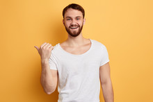 Cheerful Handsome Joyful Man Pointing With Thumb On Copyspace Behind His Back Isolated On Yellow Background. Close Up Portrait. Look Here, This Way, Please, Direction