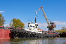 Tugboat With Row Of Black Tires Used As Boat Bumpers In Harbor Near Port Crane