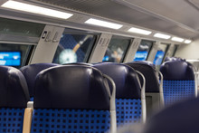 Seats In A Second-class German Regional Double-decker Train; The Train Has Arrived To The Station - A Clock And An Informational Digital Display Are Seen Behind The Window