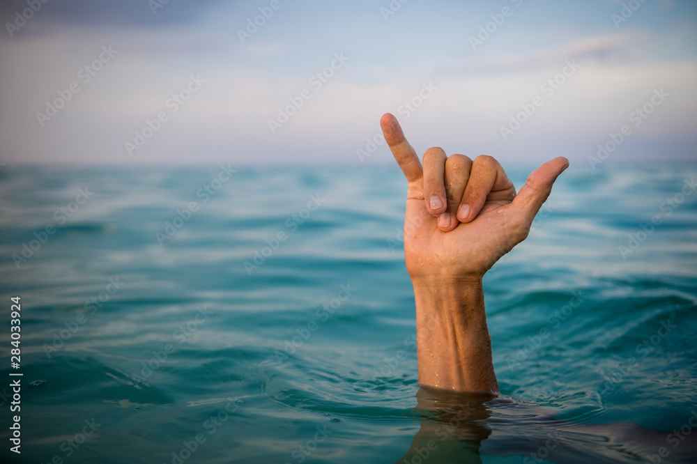 Hand of surfer making shaka (hang loose) sign in tropical blue waters - obrazy, fototapety, plakaty 
