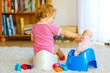 © Irina Schmidt - Closeup of cute little 12 months old toddler baby girl child sitting on potty. Kid playing with doll toy. Toilet training concept. Baby learning, development steps