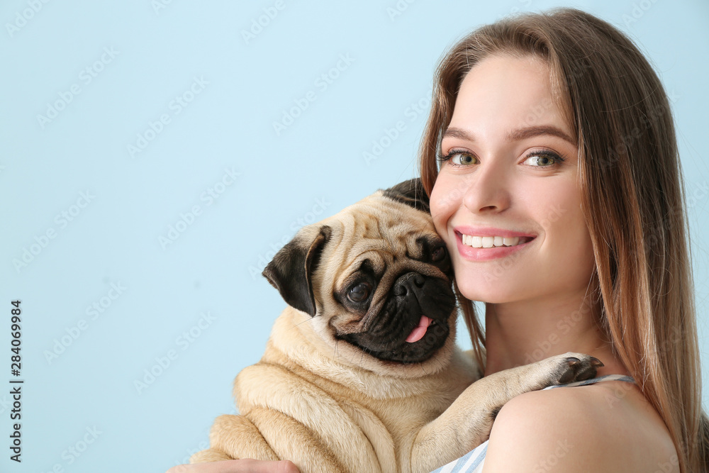 Beautiful young woman with cute pug dog on color background - obrazy, fototapety, plakaty 