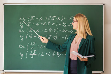 Canvas Print - Beautiful math teacher with book and pointer near blackboard in classroom