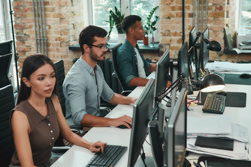 Teamwork . Group of young employees working on computers while sitting in modern open space