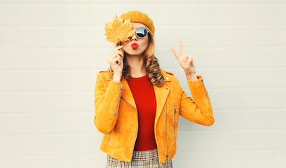 Autumn mood! woman holding in her hands yellow maple leaves hiding her eyes over gray wall background