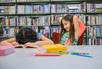 Happiness two cute diversity girls reading book and teasing to hit sleeping friend in school library funny. People lifestyle and Education and friendship. Child and kids group activity leisure