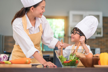 Happy beautiful Asian woman and cute little boy with eyeglasses prepare to cooking in kitchen at home. People lifestyles and Family. Homemade food and ingredients concept. Two Thai looking each other